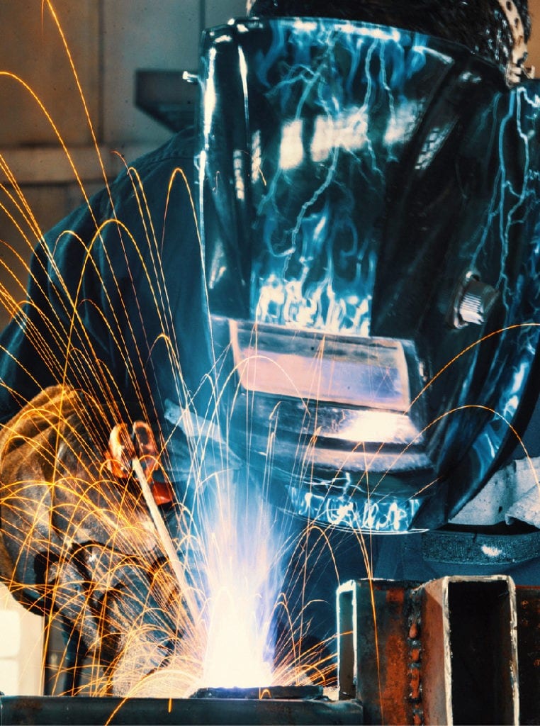 Welder with helmet in manufacturing facility
